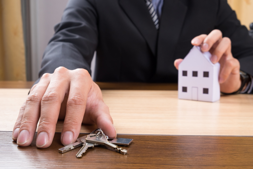 A man in a suit holding a house key in one hand and a miniature house in the other—symbolising property ownership or real estate transactions in the UK.
