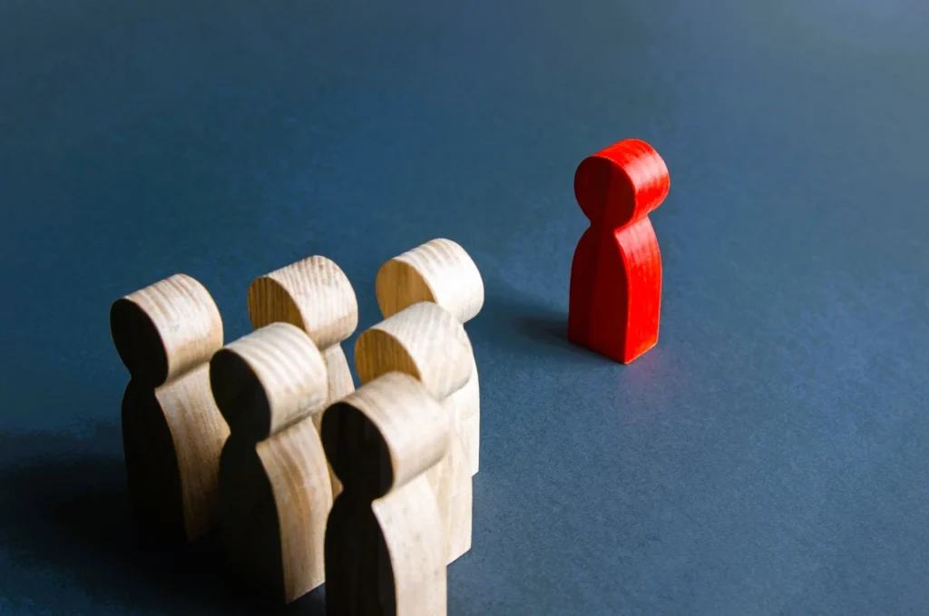 Red wooden figure separated from a group of neutral figures, symbolising workplace discrimination and equality law in the UK.