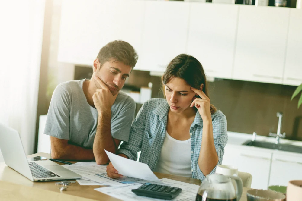 Couple reviewing unpaid invoices and financial documents at home, symbolising debt recovery and legal enforcement services in the UK.