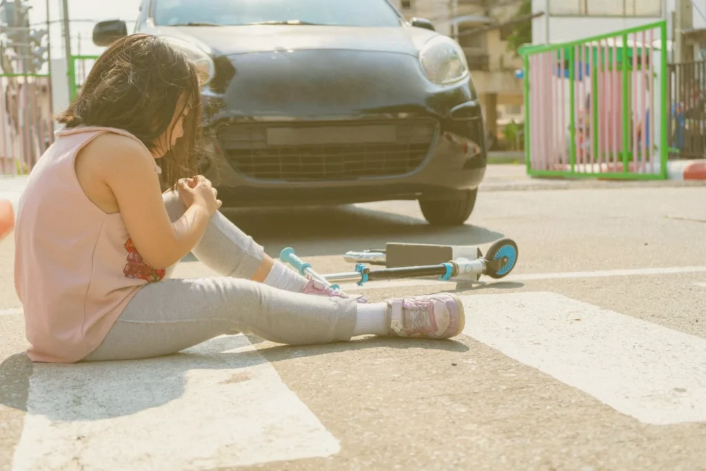 A pedestrian young girl fell of her scooter, and a car on the background which possibly hit her