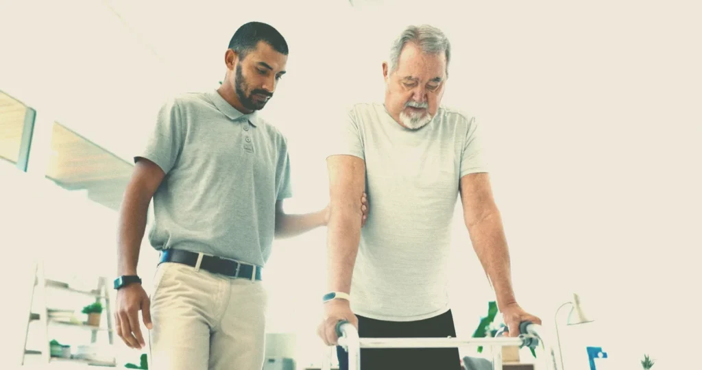 A young man helping an old man to walk in rehabilitation after a serious accident