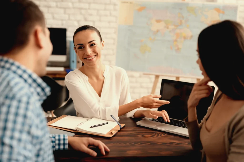 A woman showing the laptop screen, helping a couple to get skilled worker visa to move to the UK.