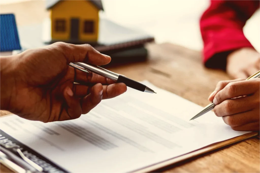Two people discussing and signing a will document with a house model in the background