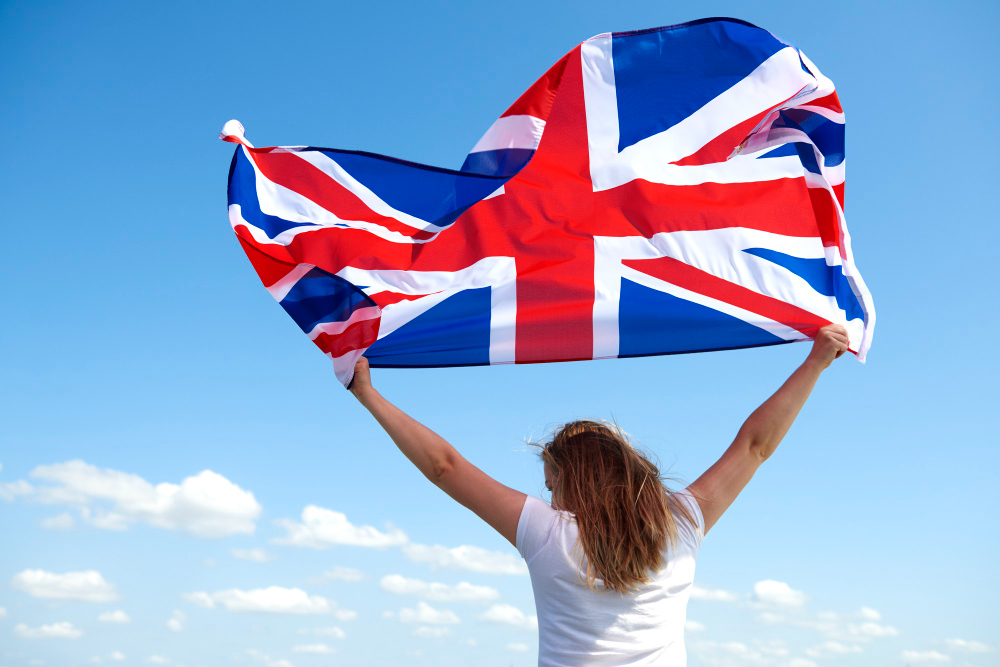 A woman holding the UK flag above her head under a blue sky—symbolising freedom, national pride, or new beginnings in the United Kingdom